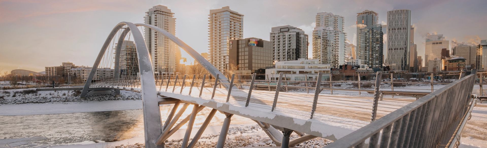 The contemporary George C. King pedestrian bridge over the Bow River in winter at sunrise with Calgary's downtown behind
