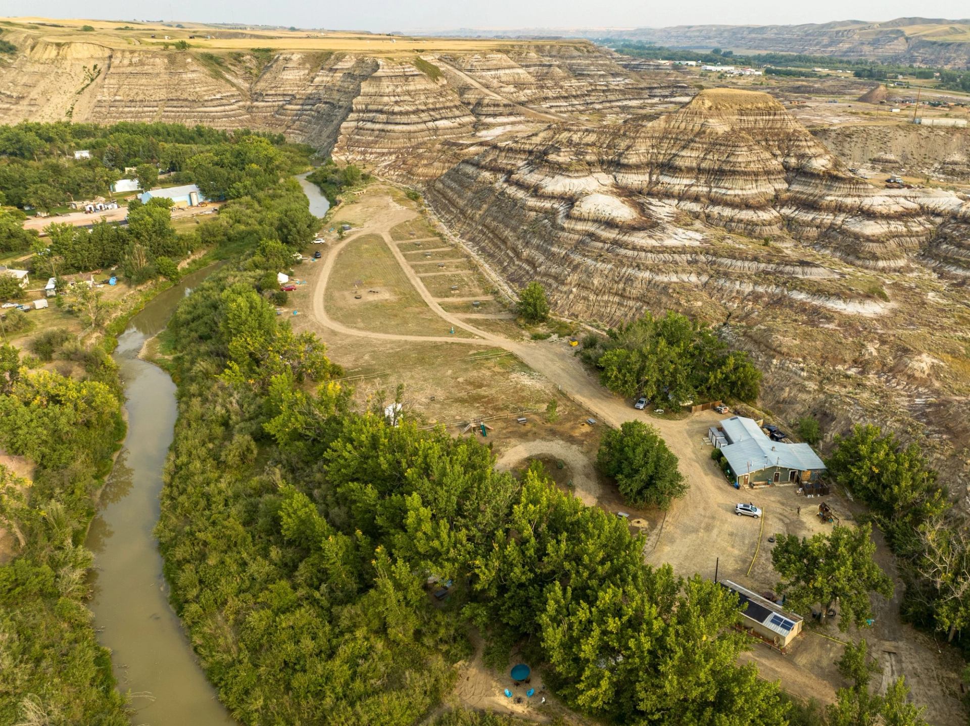 A bird’s-eye view of Bridgeviews Retreat & Glamping with the geology of the Canadian Badlands and a small river.