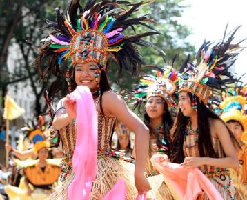 Female dancers in colourful costumes with one smiling at the camera during an outdoor festival performance.