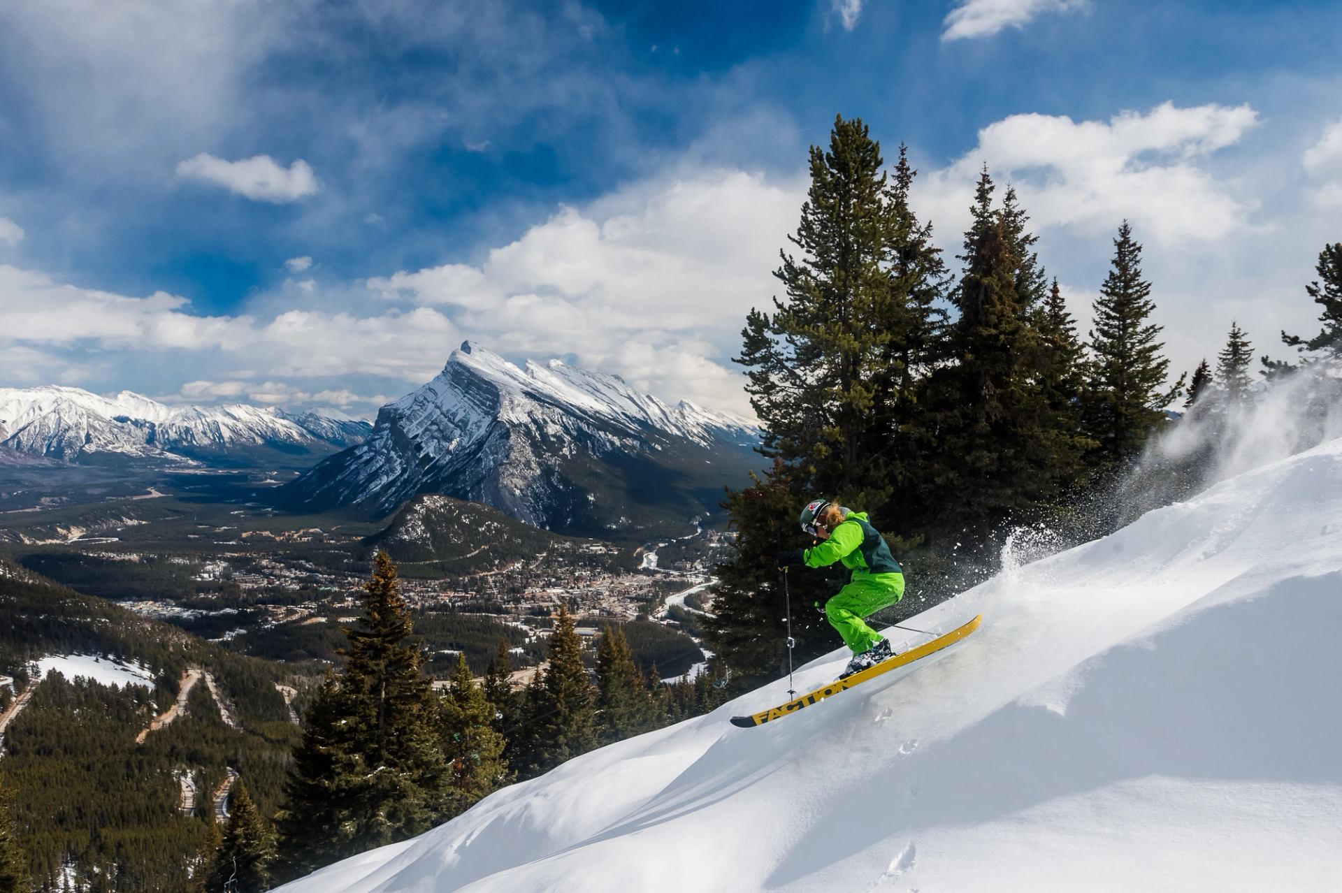 A skier in fresh powder at Mount Norquay with Banff townsite and Rocky Mountains in the background.