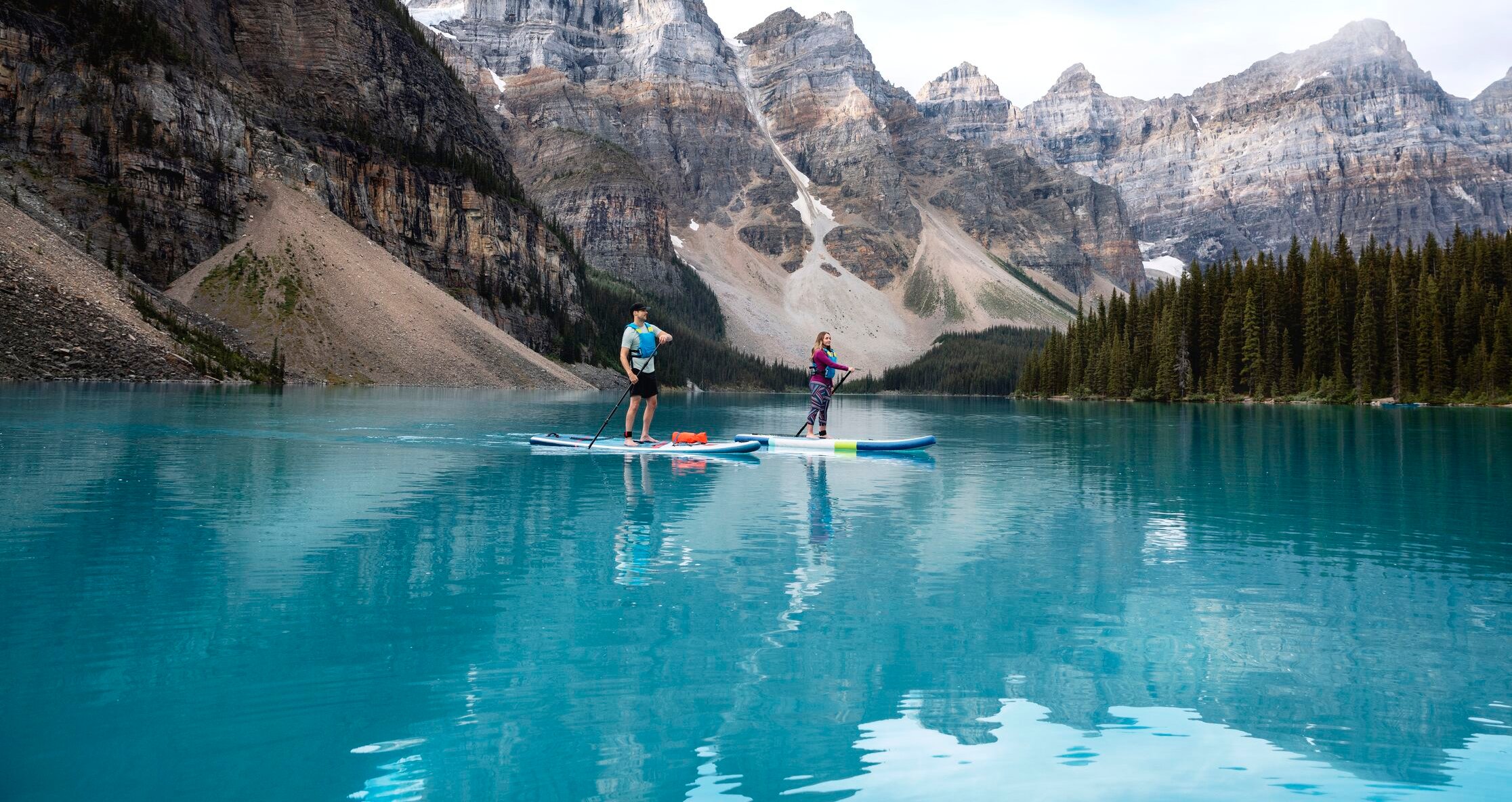 Two people paddleboarding on a glacial lake.