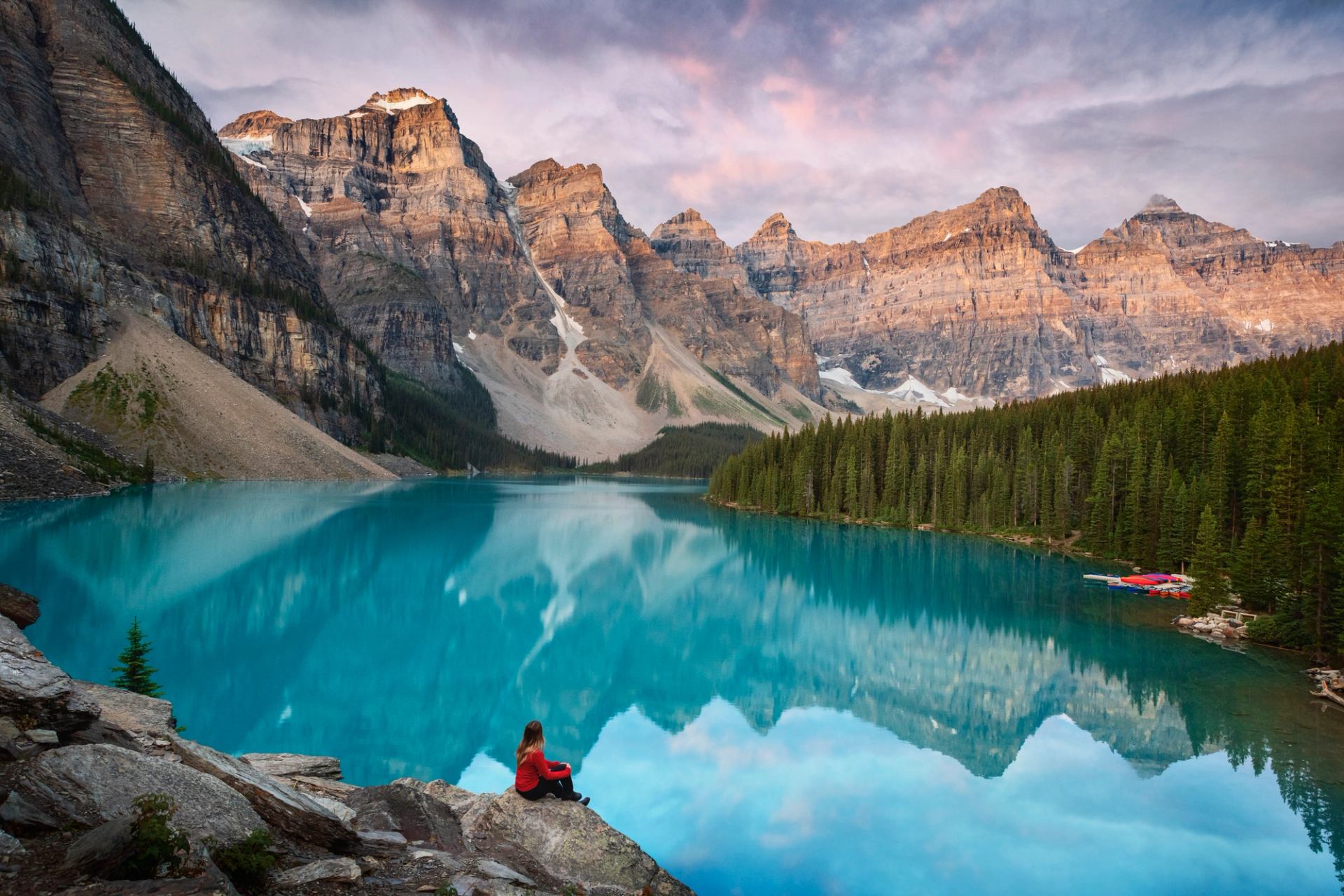 Hiker sitting down and looking out on a breathtaking turquoise coloured lake with an epic mountain backdrop