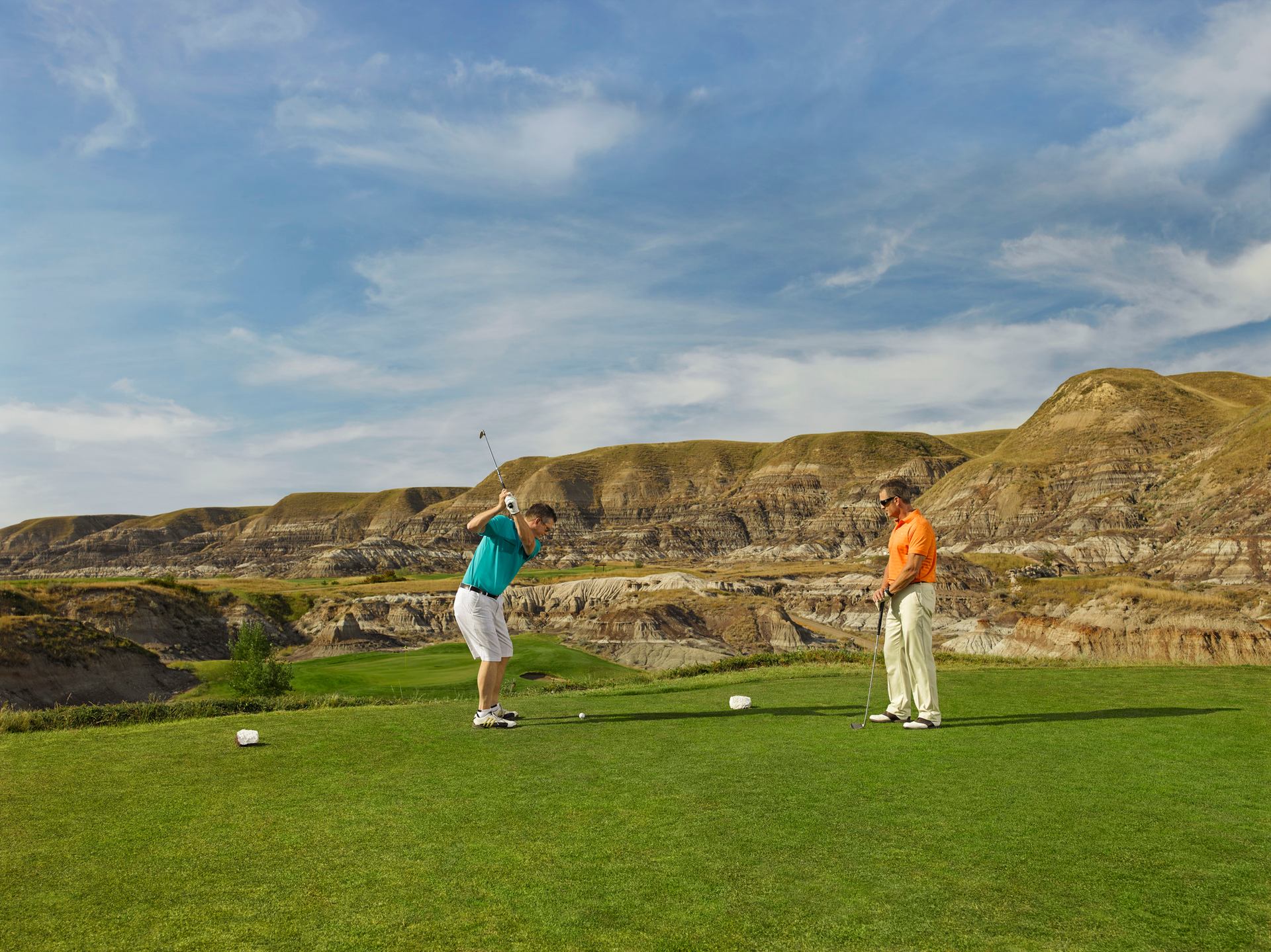 Two men golf on a course in the badlands.