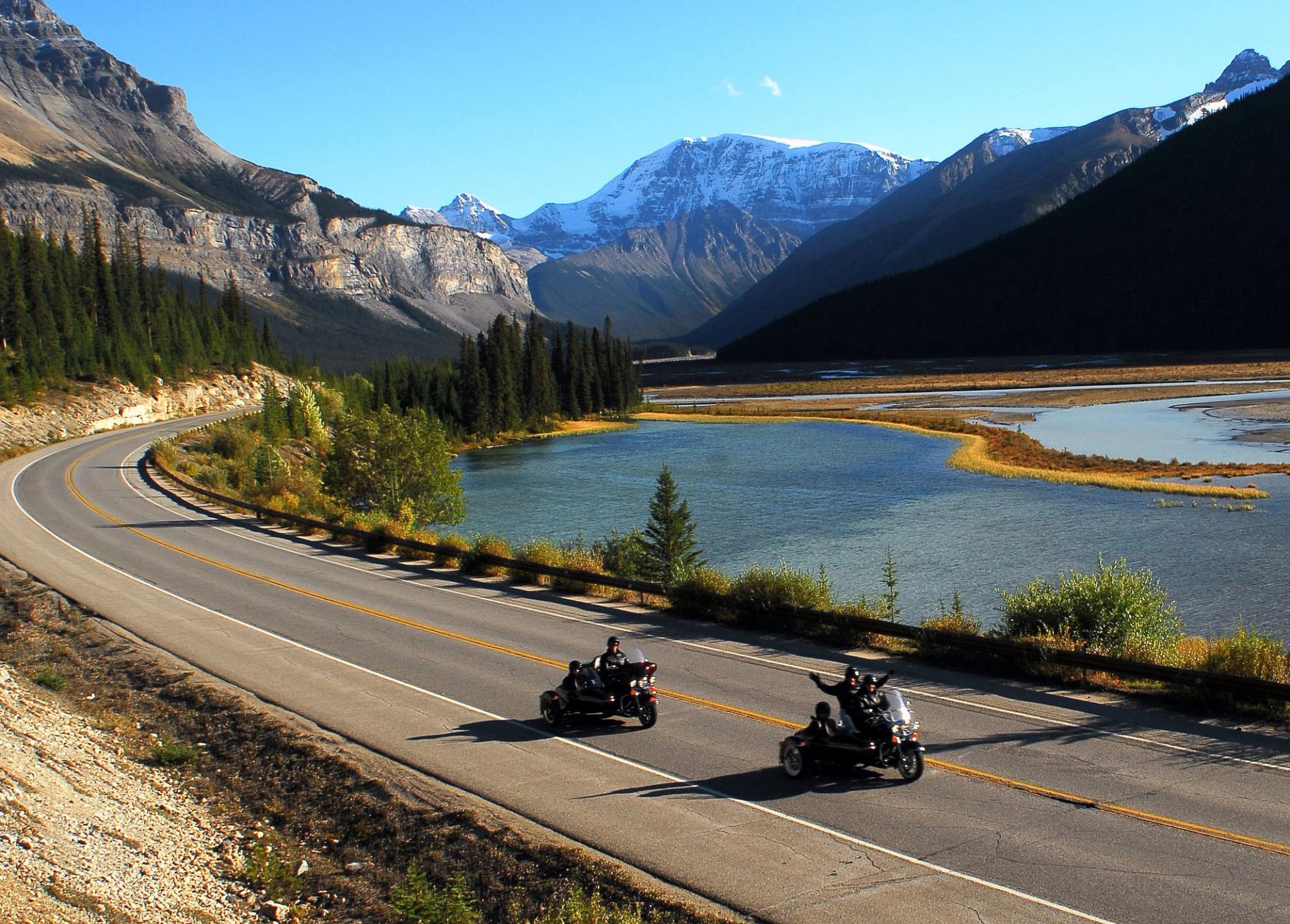 Travellers are ready to ride in vintage motorcycles and their sidecars with blue skies in the background.