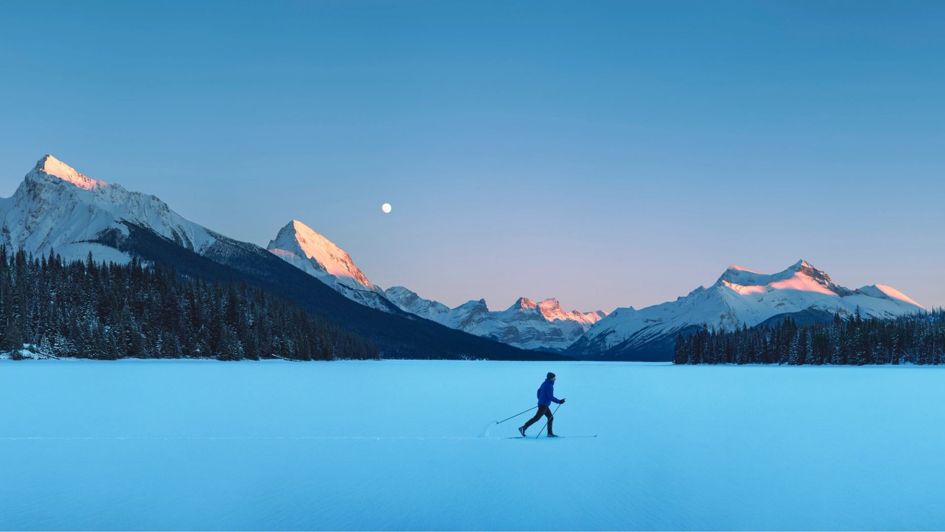 A panoramic shot of a man cross-country skiing on Maligne lake.