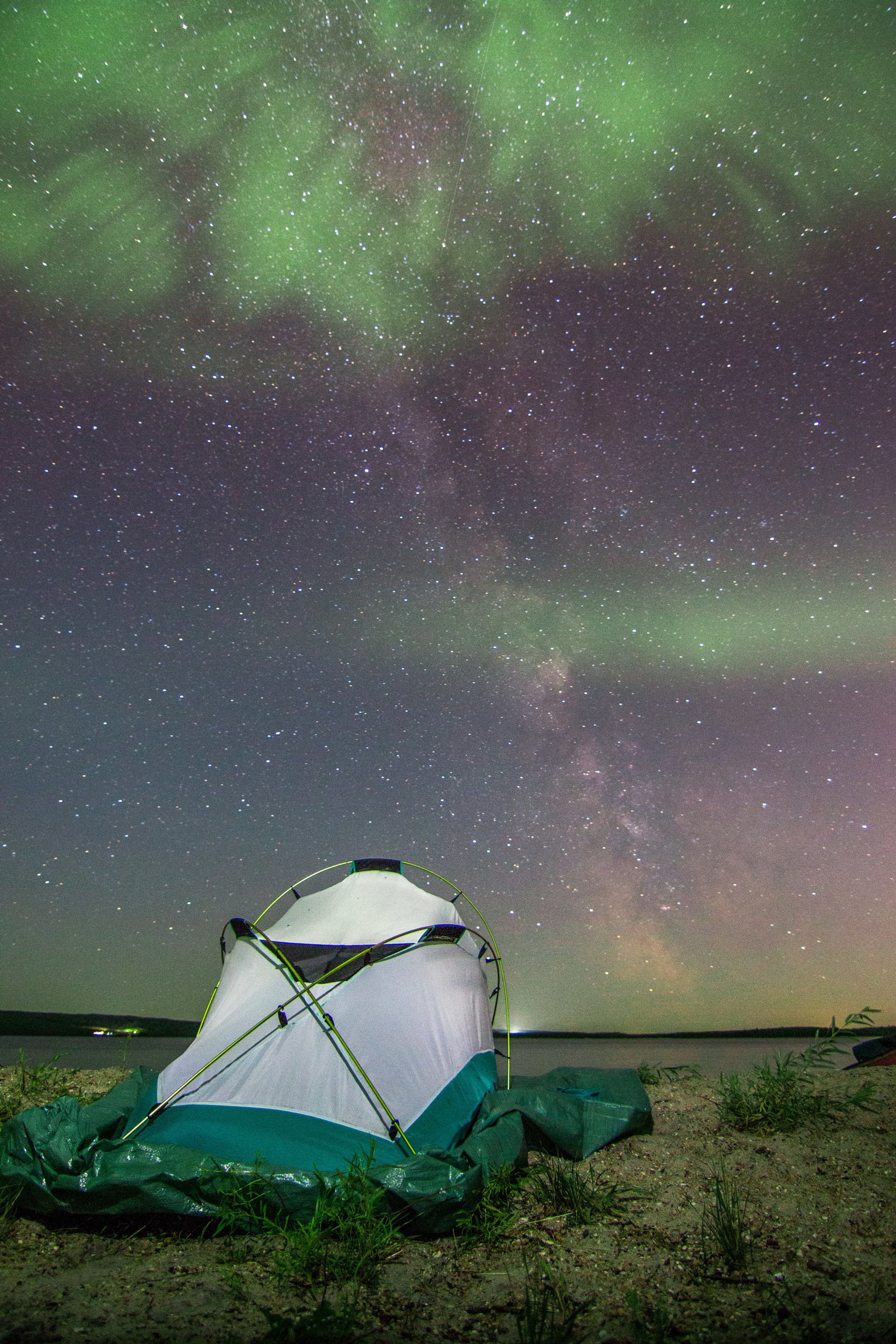 Northern Lights in the nights sky above a camping tent at a lake shore.