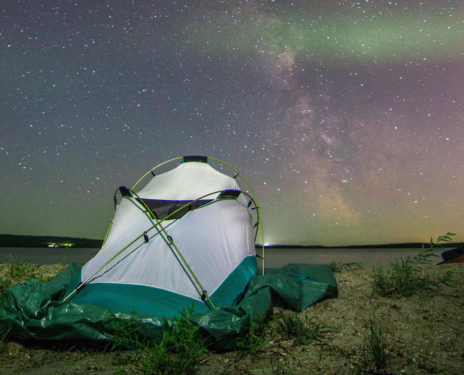 Northern Lights in the nights sky above a camping tent at a lake shore.