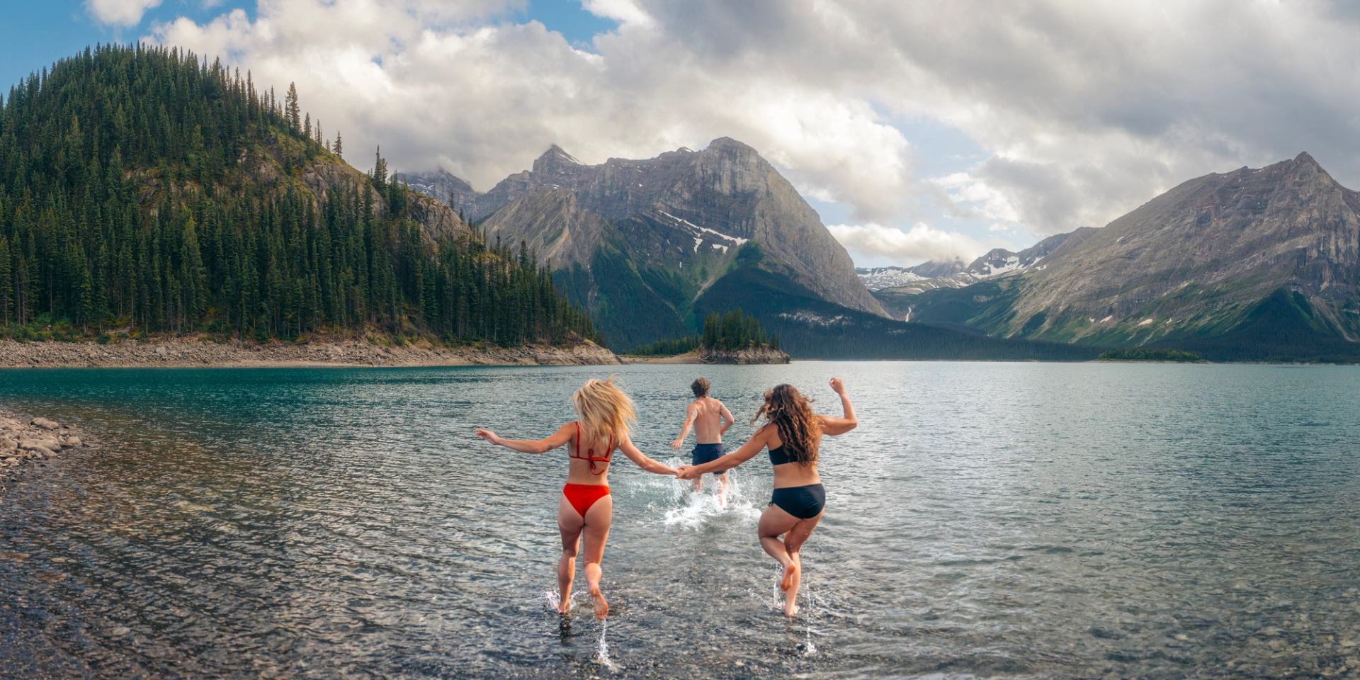 Three people running into the glacier-fed Upper Kananaskis Lake.