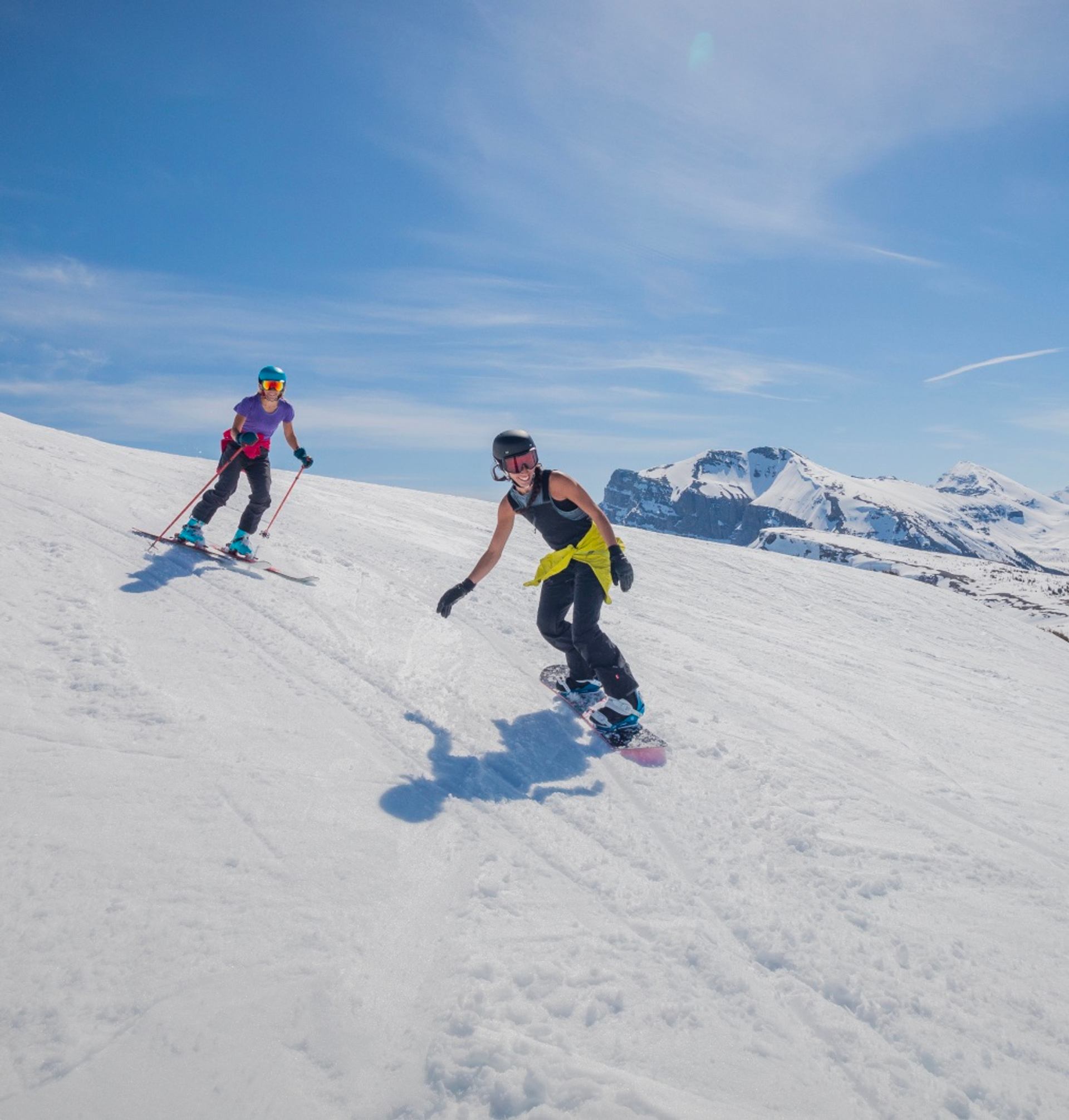 A skiier and snowboarder riding downhill on a sunny winter day.