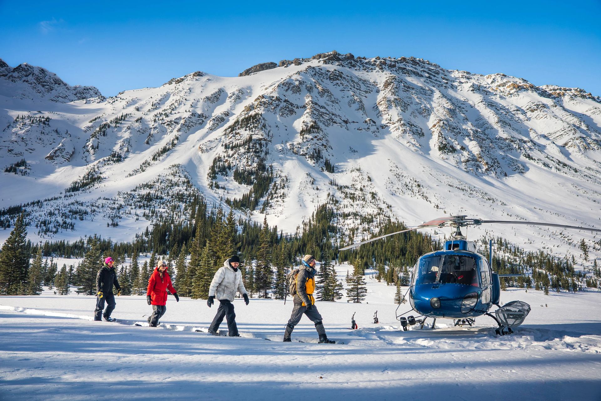 Guests snowshoe past a helicopter in a snowy mountain valley in Alberta.