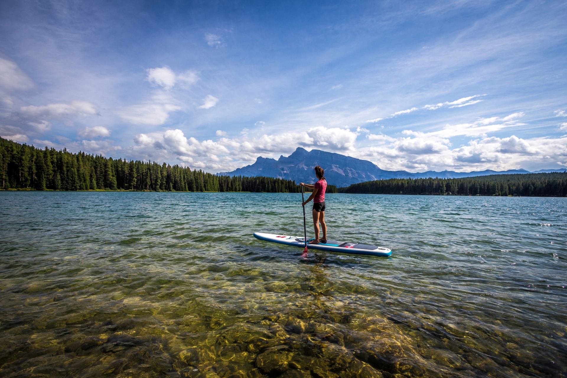 A paddler on a stand-up paddleboard calmly floats on blue-green water with a mountain in the distance