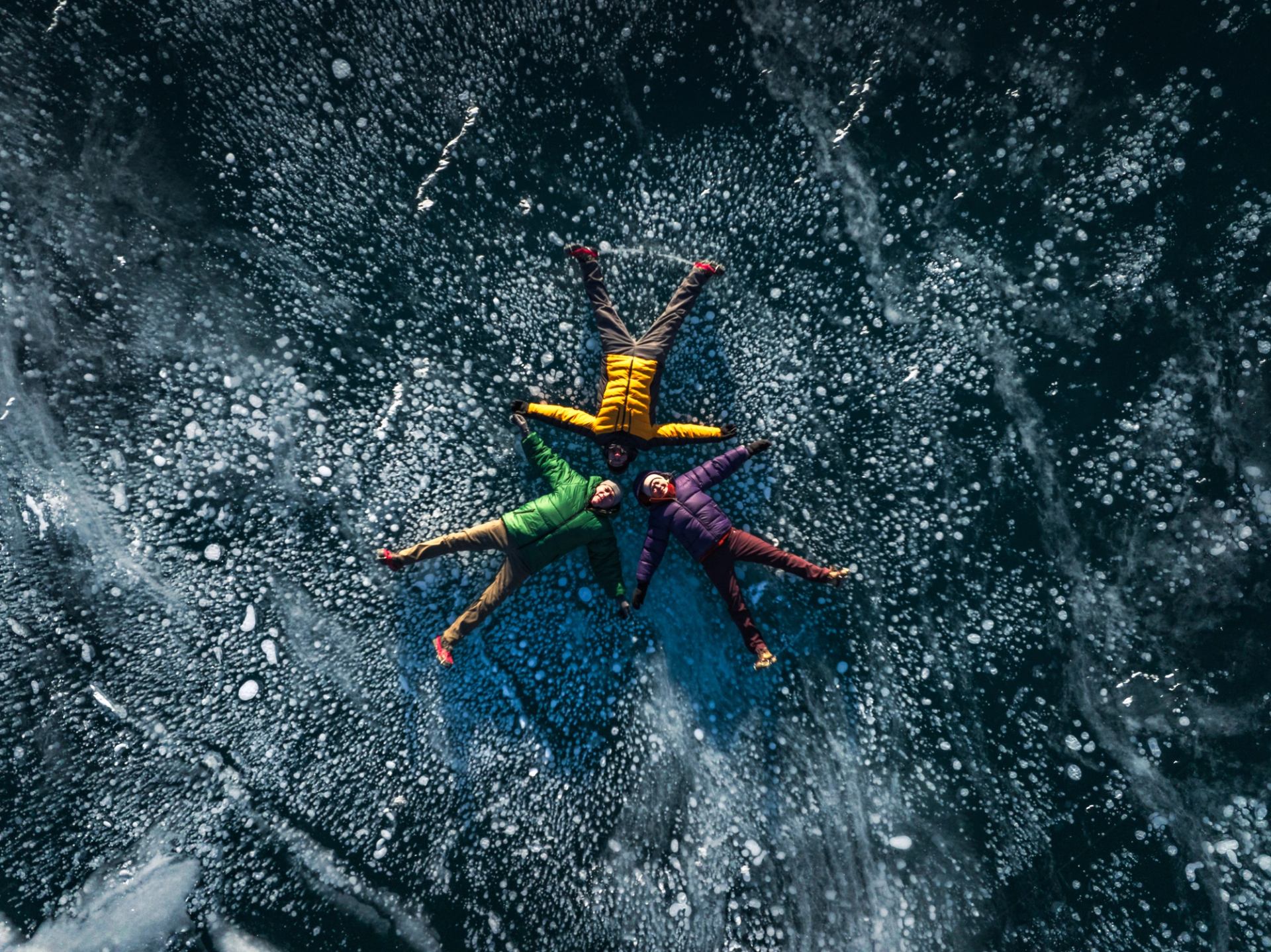 Couple with guide laying on a frozen surface surrounded by ice bubbles at Abraham Lake.
