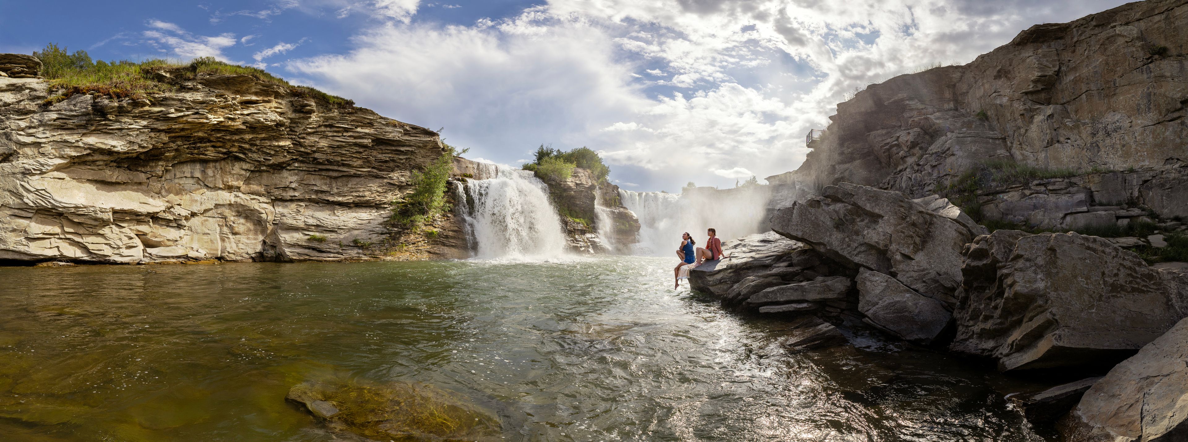 Two women admire Lundbreck Falls from the rocks at the base of the falls