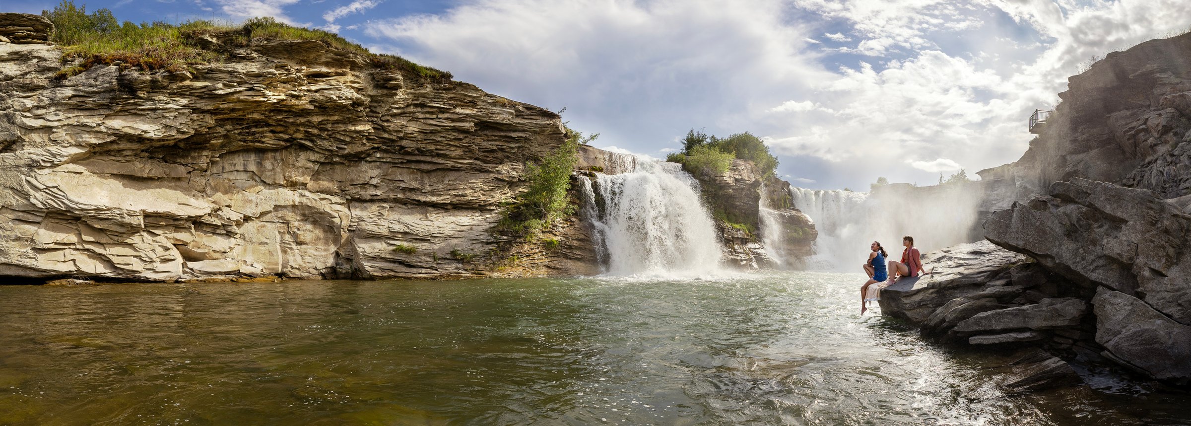 Two women admire Lundbreck Falls from the rocks at the base of the falls