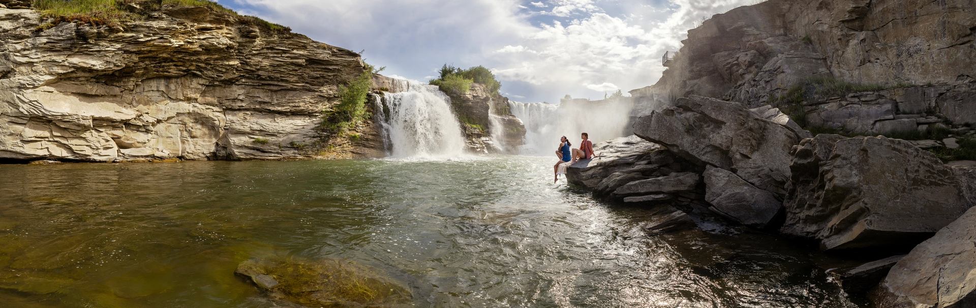 Two women admire Lundbreck Falls from the rocks at the base of the falls