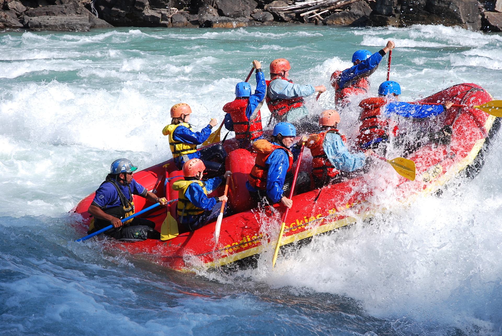 Group getting splashed by water as the whitewater rafting boat rides into a wave.