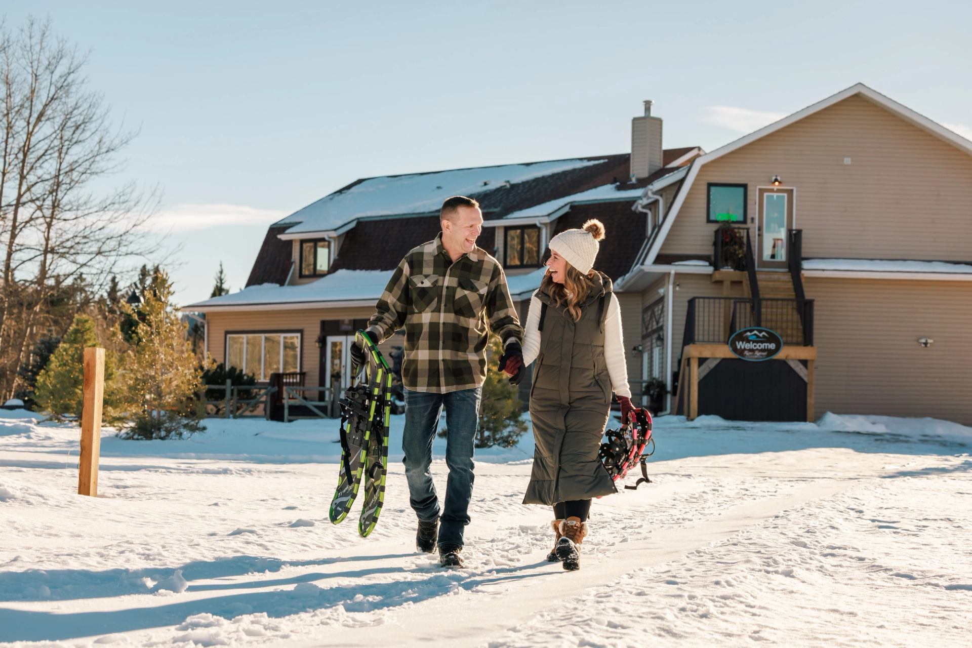 A couple holds hands and snowshoes as they walk in the snow away from the main building at River Retreat Kananaskis.