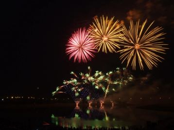 Fireworks at night over a reflective lake.