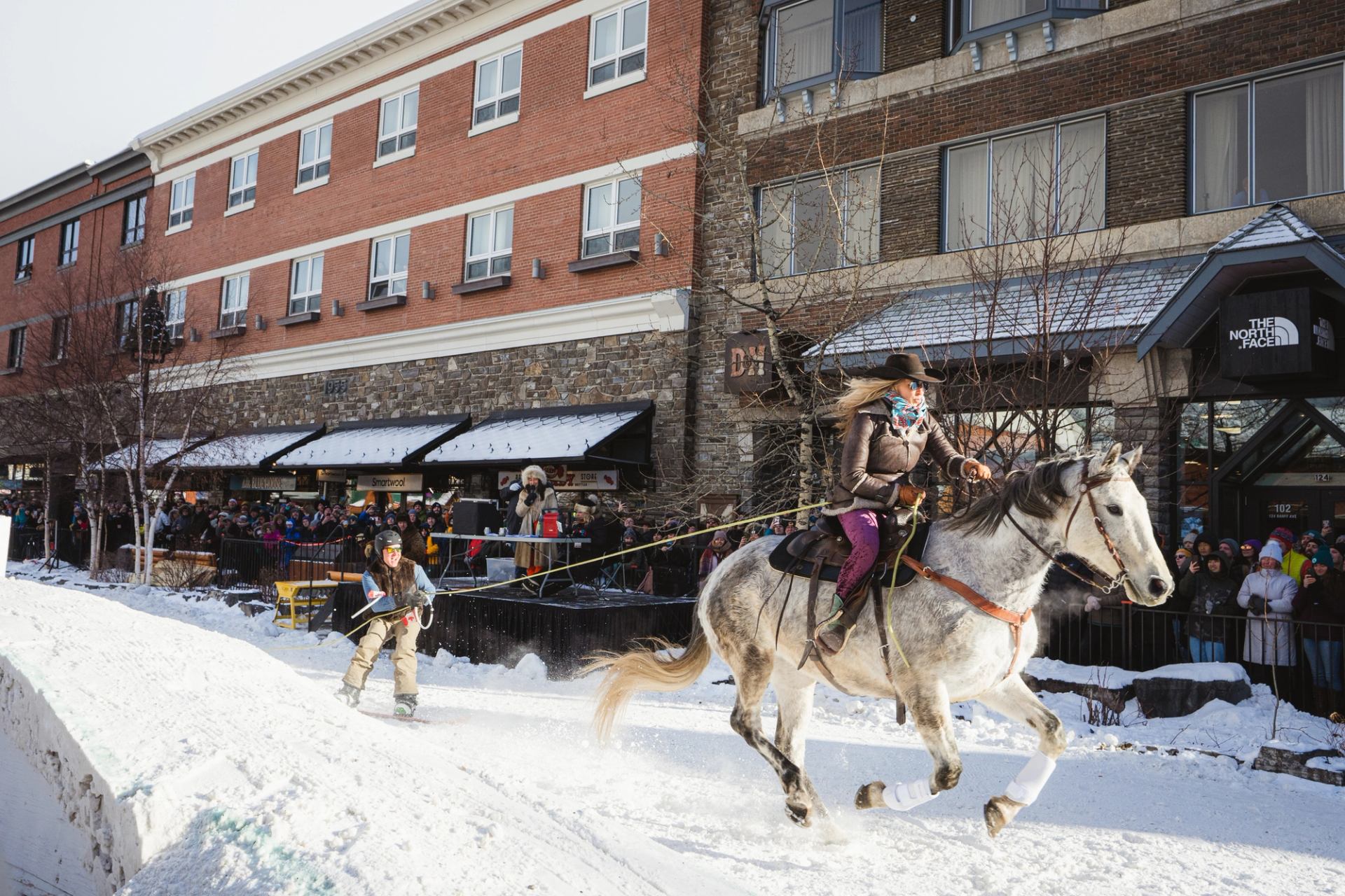 Spectators line the street while enjoying a skijoring event during a winter festival.