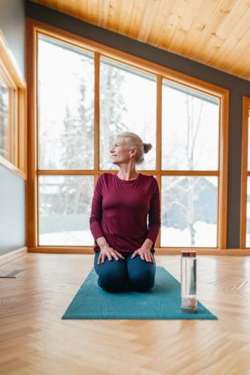 A woman kneels on a yoga mat and looks into the distance in a minimalist yoga studio.
