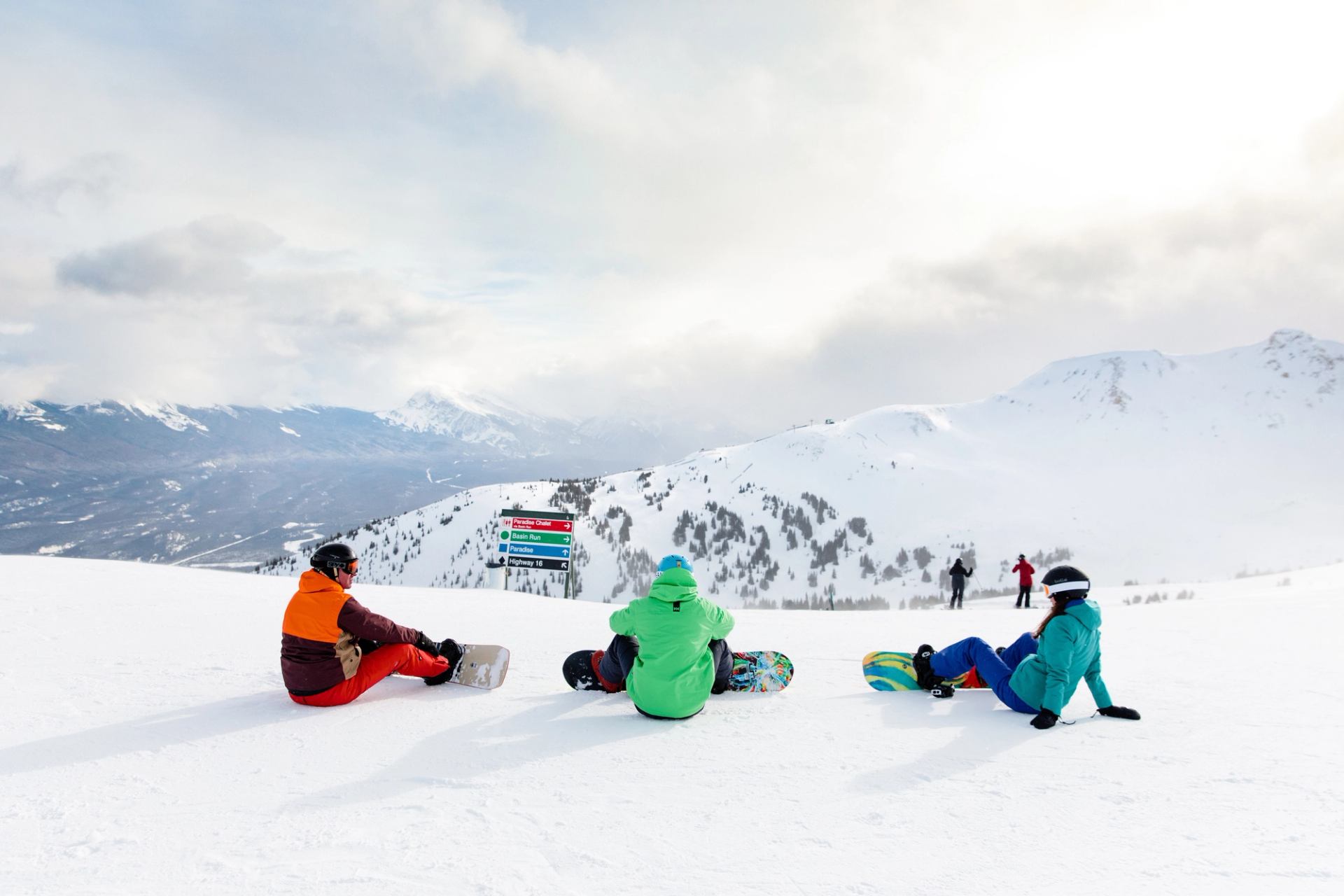 Three snowboarders sit down overlooking a run before snowboarding at Marmot Basin in Jasper National Park