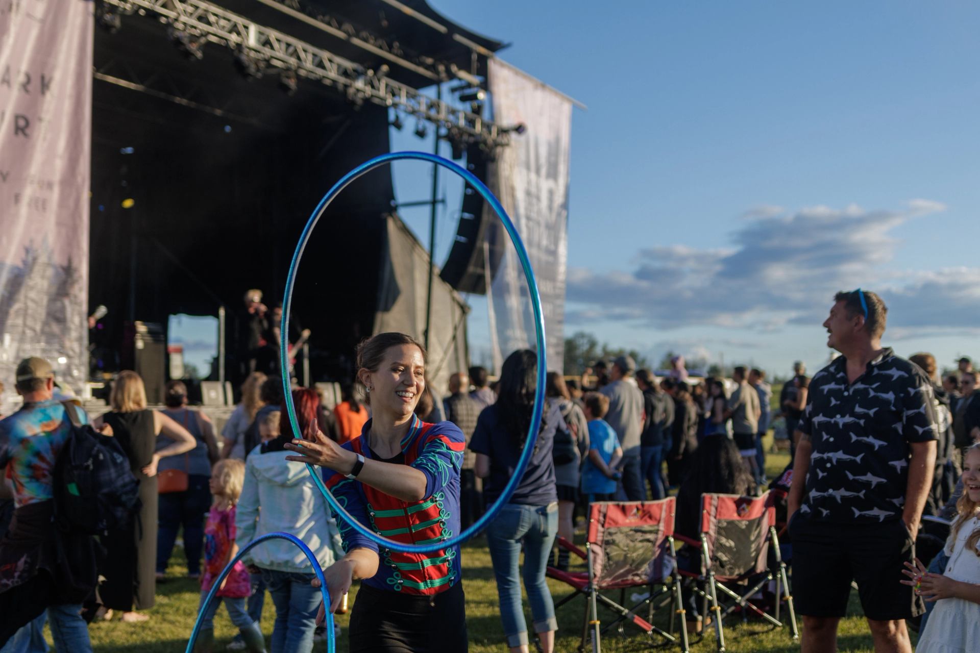 A performer with hula hoops in the crowd at a music festival, with the stage behind them.