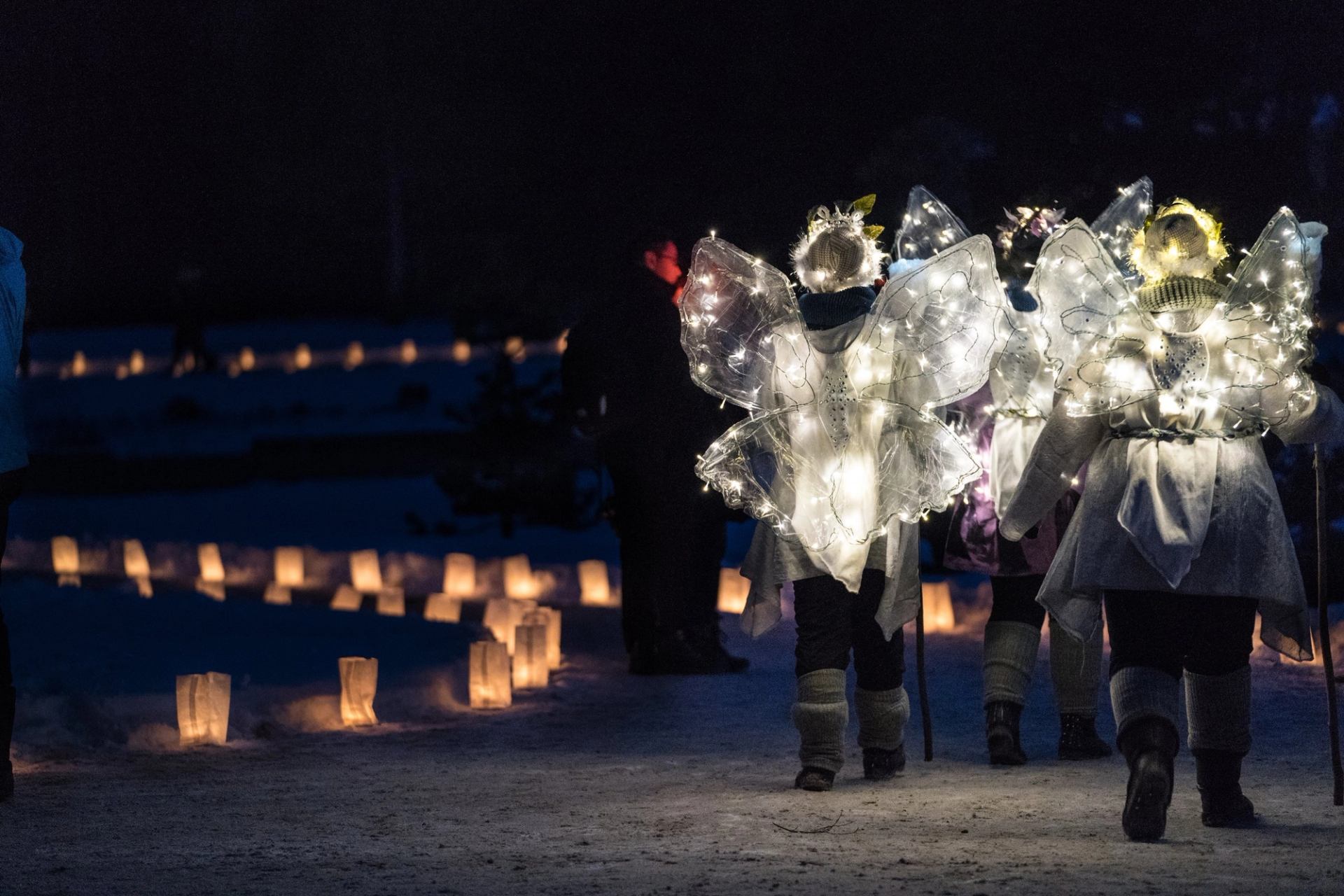 Illuminated angel figures stand on a snowy pathway of lights.