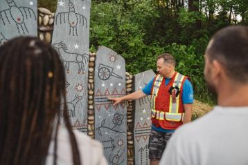 A view over the shoulders of a man and women listening to a guide showcasing painted rocks.