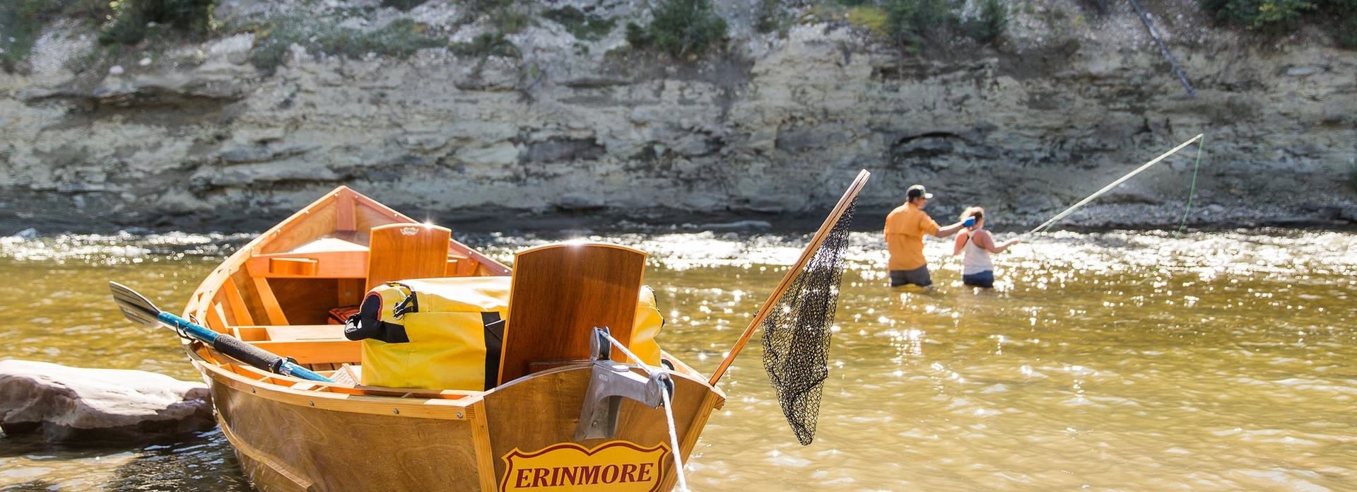 Couple learning to fly fish in a river with a boat in the foreground