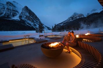 A couple relax outdoors among the pools and firepits at BASIN Glacial Waters Spa at Fairmont Chateau Lake Louise.