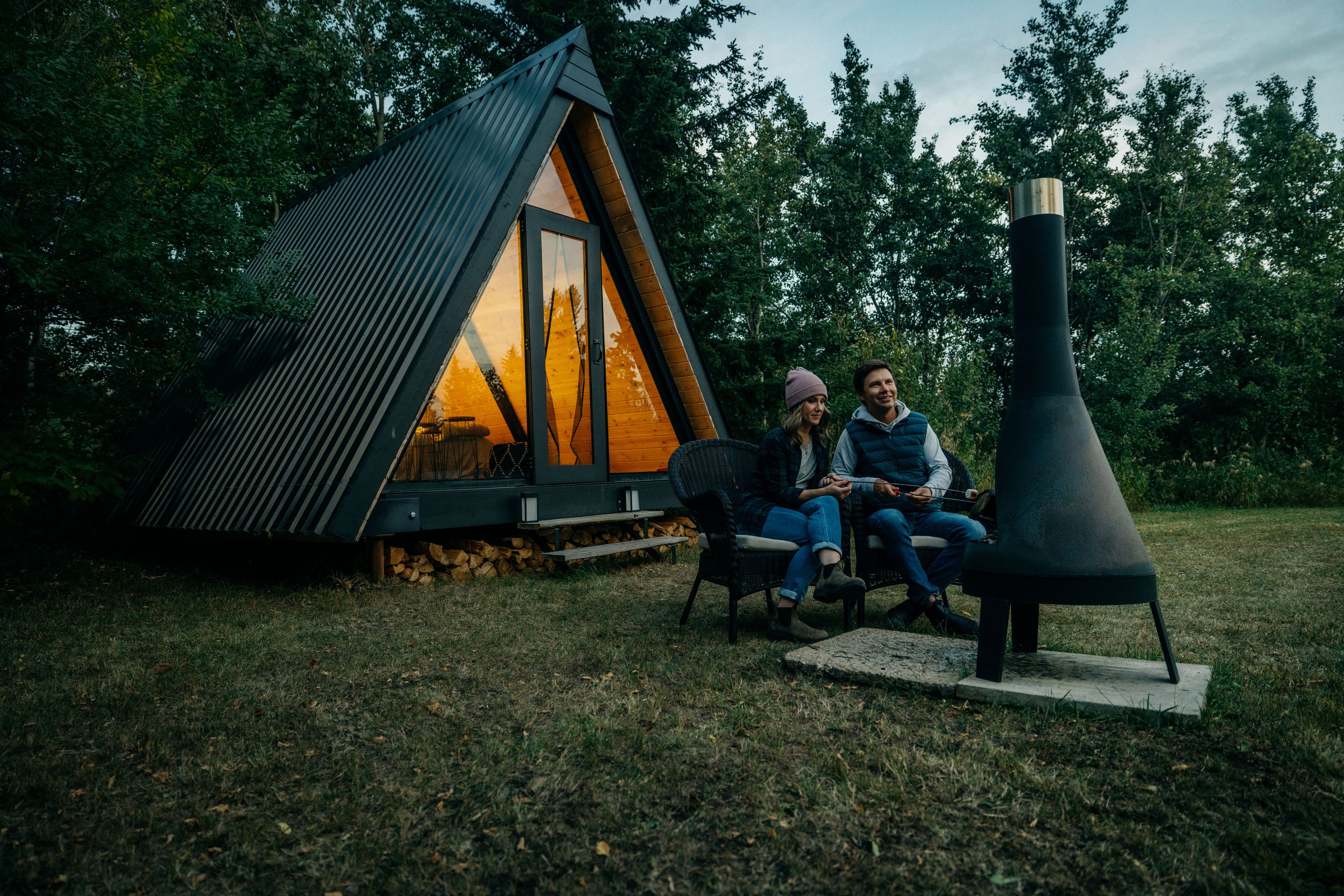 Two people roast marshmallows at Pine Creek Retreat in front of an A-frame cabin.