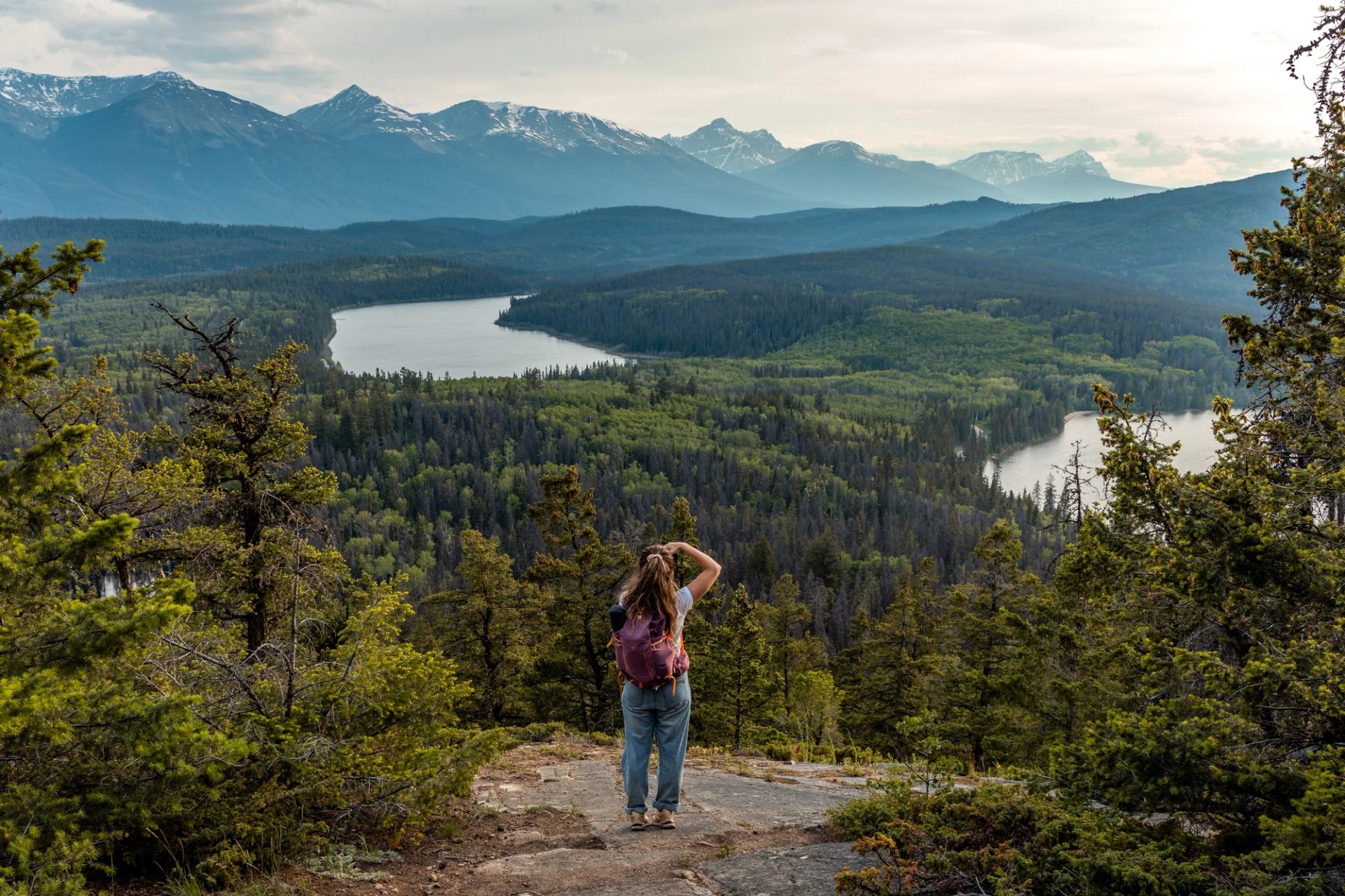 A hiker takes a photo on a mountain trail in Jasper with Patricia Lake in the distance.
