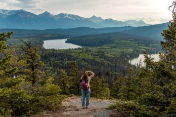 A hiker takes a photo on a mountain trail in Jasper with Patricia Lake in the distance.