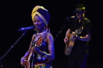 Two music performers singing and playing guitar on a dark stage