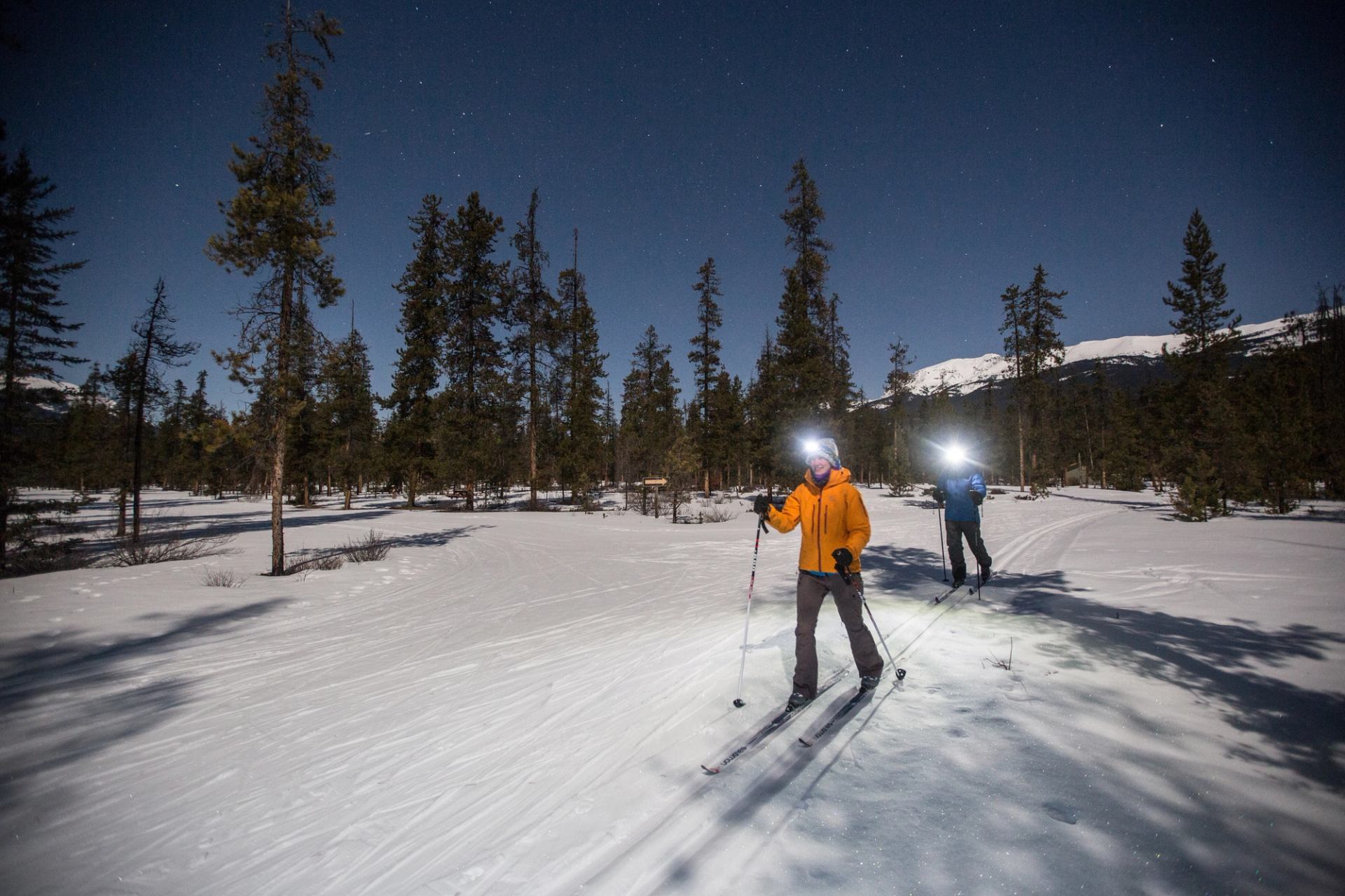 Two people cross country ski at night with headlamps in Jasper National Park.