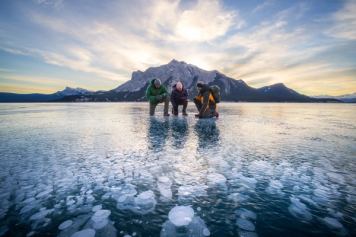 A couple with a guide enjoying ice bubbles at Abraham Lake.