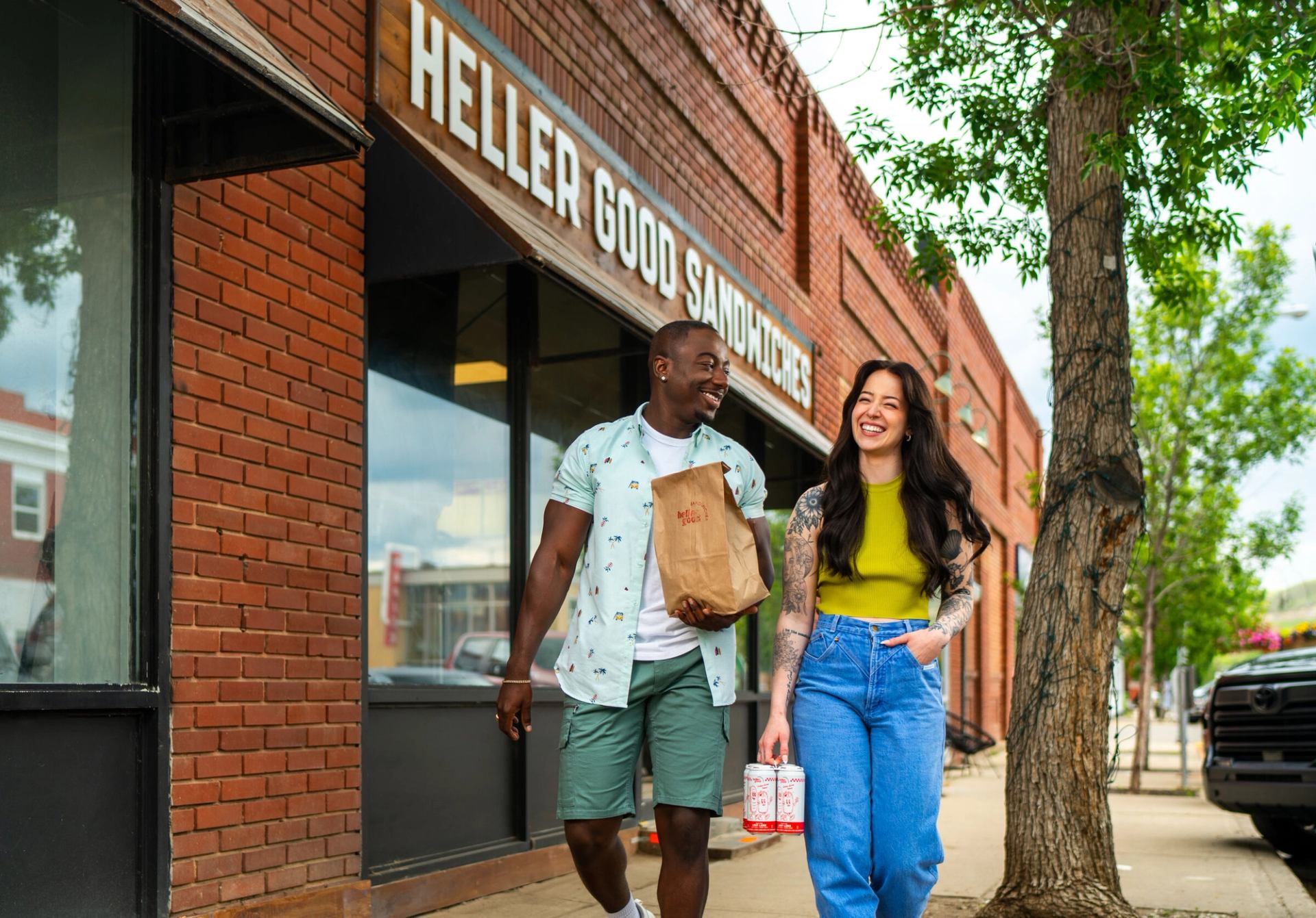Two people take sandwiches to go as they walk away from the Heller Good Sandwiches storefront.