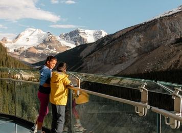 Two male kids standing along a clear glass railing of a skywalk overlooking a mountain view.