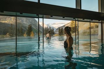 Two people enjoying the indoor/outdoor pools at BASIN with the Rocky Mountains in the background.