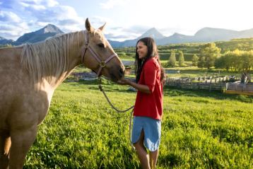 A young women laughs and pets a horse at the Thanksgiving Ranch