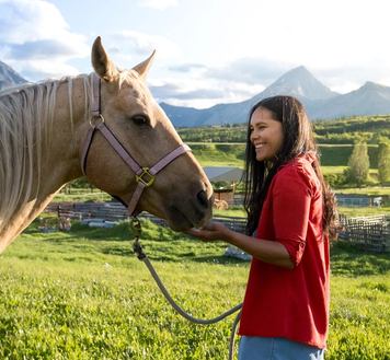 A young women laughs and pets a horse at the Thanksgiving Ranch
