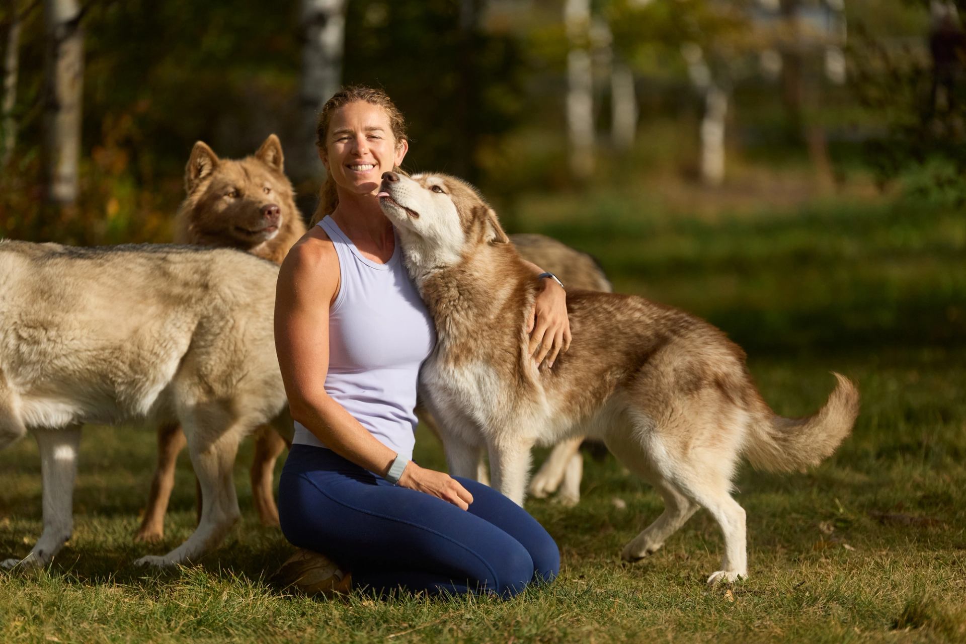 The owner of Yamnuska Wolfdog Sanctuary posted with a pack of young wolfdogs while one licks her face.