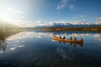 A family canoes on Pyramid Lake in Jasper, surrounded by the Canadian Rockies and green and gold pine trees