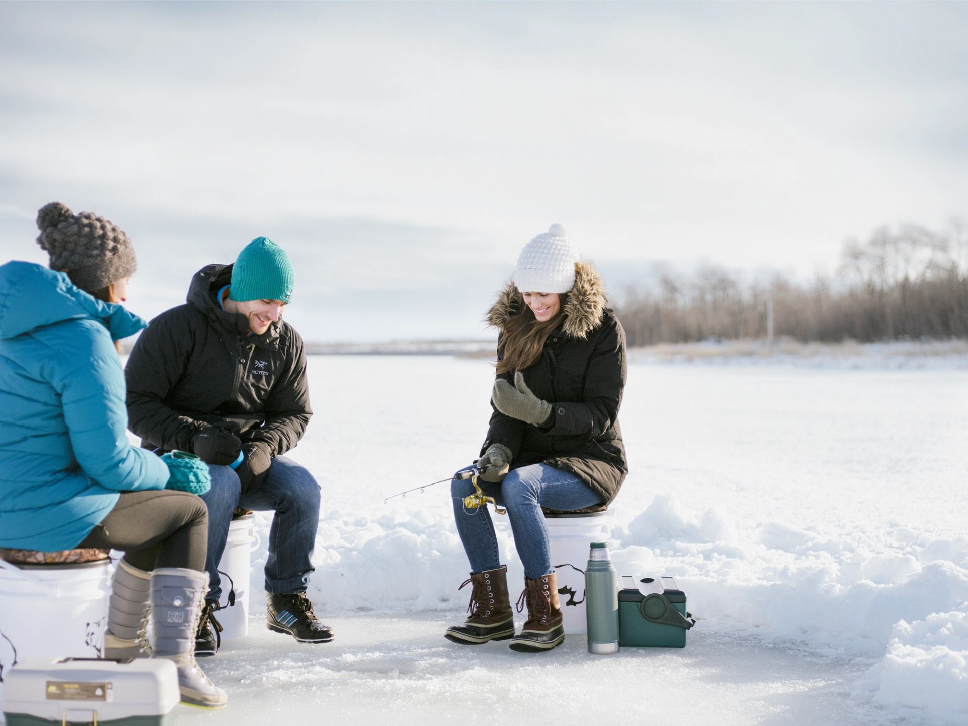 Close-up of friends ice fishing while sitting on a frozen Bear Lake near Grande Prairie