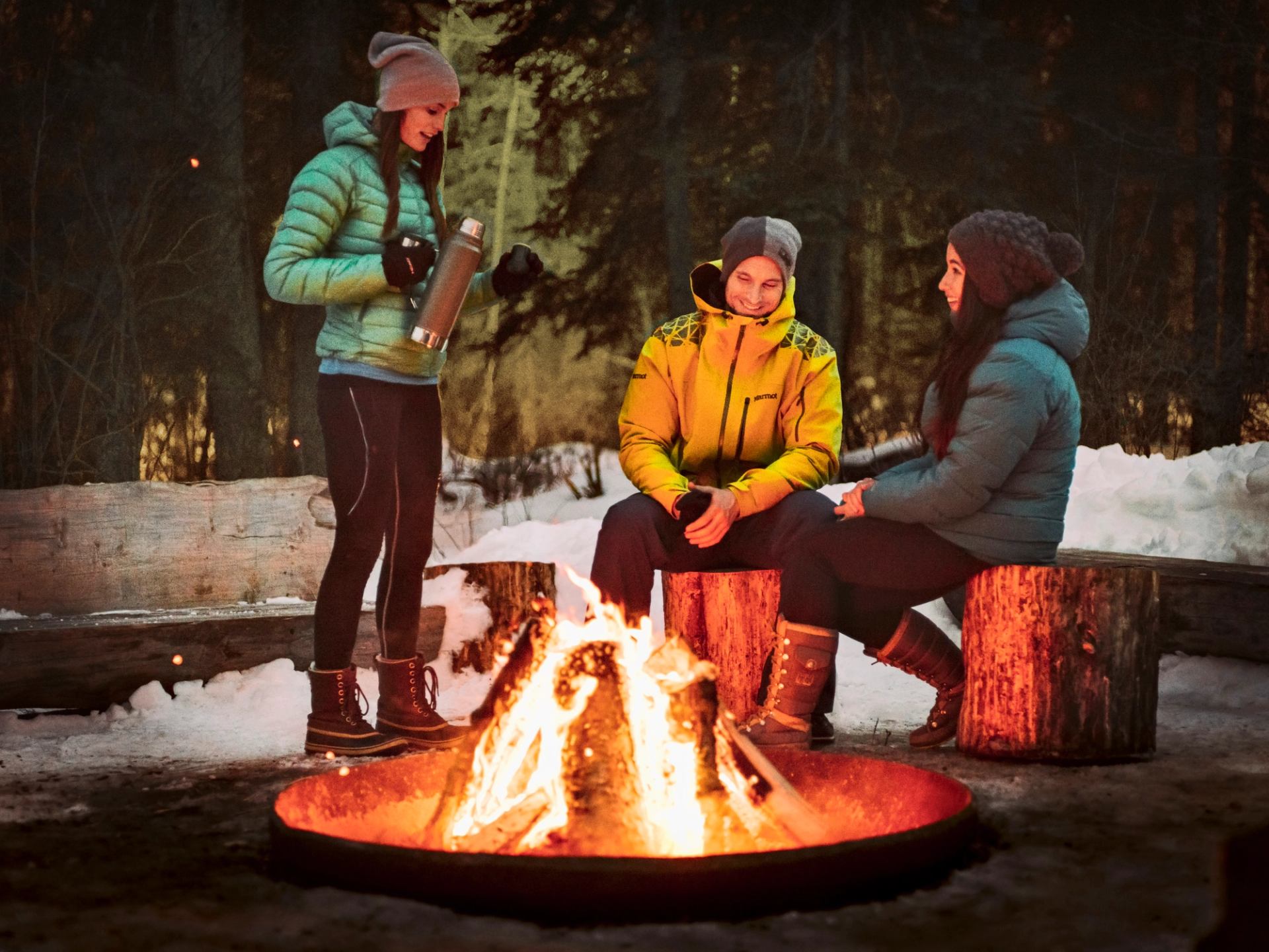 Friends having a hot drink around a campfire at night.