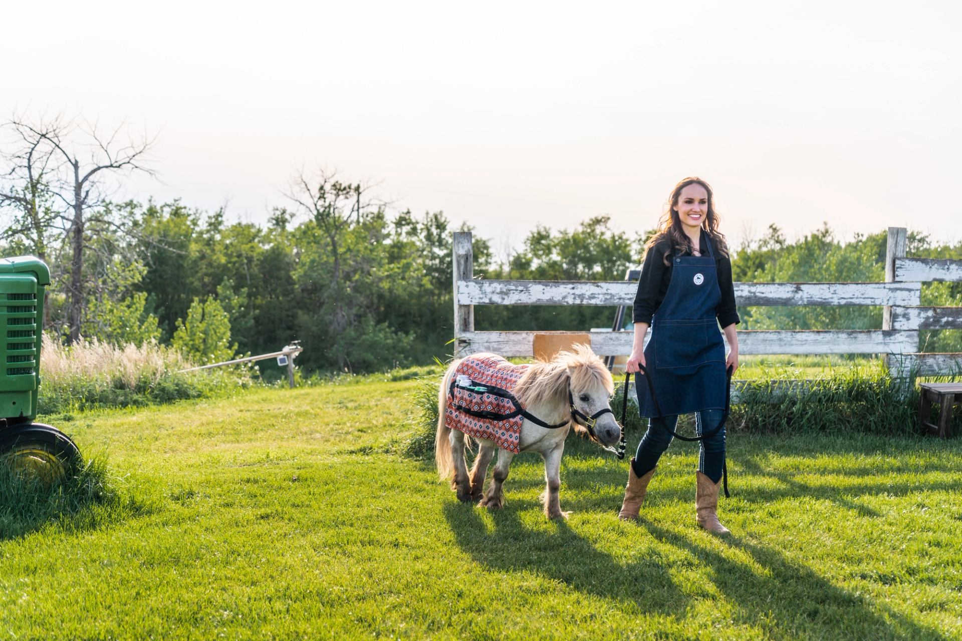 A woman leads a small pony through a farmyard.