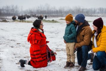 Métis Interpreter talks to a child and his parents in front of a herd of bison.