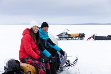 Couple sitting on a snowmobile before ice fishing at Aurora Borealis Indigenous Village in Fort McMurray