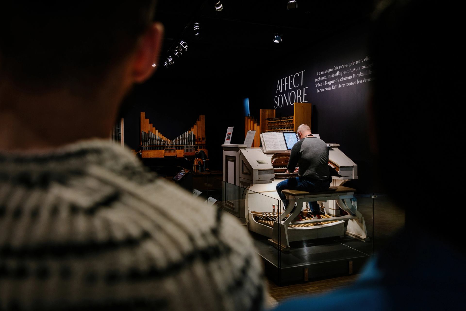 Looking over a child's shoulder watching a piano player on stage.