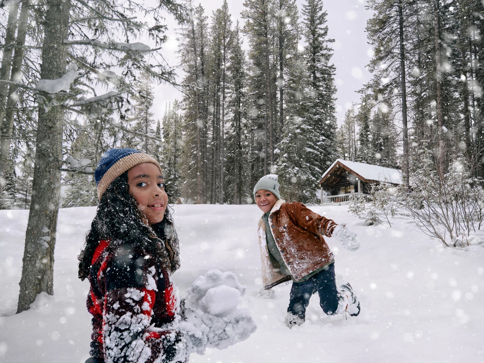 Two kids playing in the snow outside of a cabin at Storm Mountain Lodge.